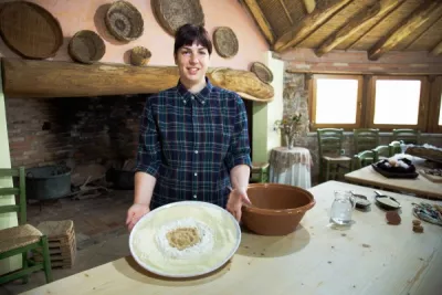 A young woman poses while smiling in a traditional farm house with a plate full of flour and spices