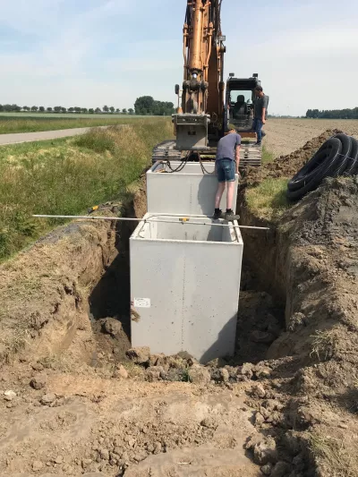 A man stands on a cement box which is placed inside a field. There is a construction machine behind him.