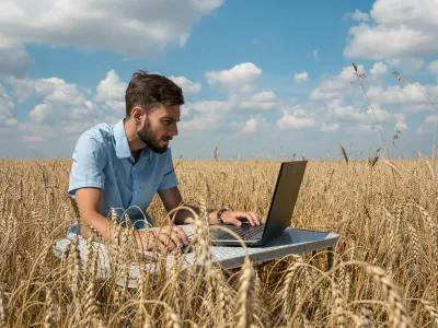 A young man works on his laptop in a field