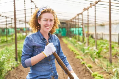 A woman with curly hair smiles at the camera inside a greenhouse