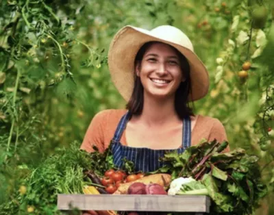 Happy young female farmer holding a basket of vegetables in a garden