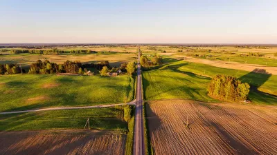 Aerial view over rural village with agricultural green fields during sundown.