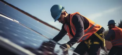 A man wearing a hard hat and vest working on solar panels