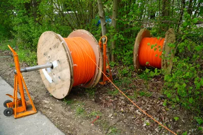 Two large wooden spools of orange cable placed outdoors near a grassy and wooded area