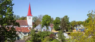 A village with colorful houses, greenery, and a church with a red steeple
