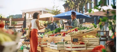 Hispanic Female Customer Buying Two Garlic Heads and a Pineapple From a Multiethnic Farmers Couple