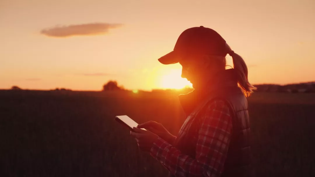 a woman in a hat and a backpack looking at a tablet in front of the sunset for 'Women in the new CAP'