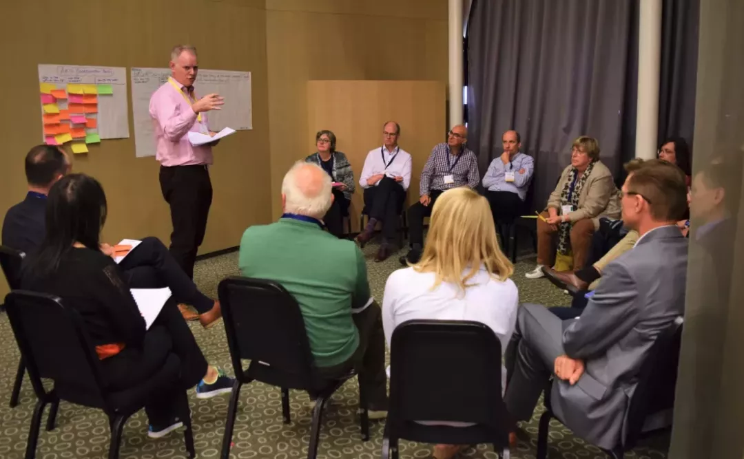 A group of people listen to a speaker presenting