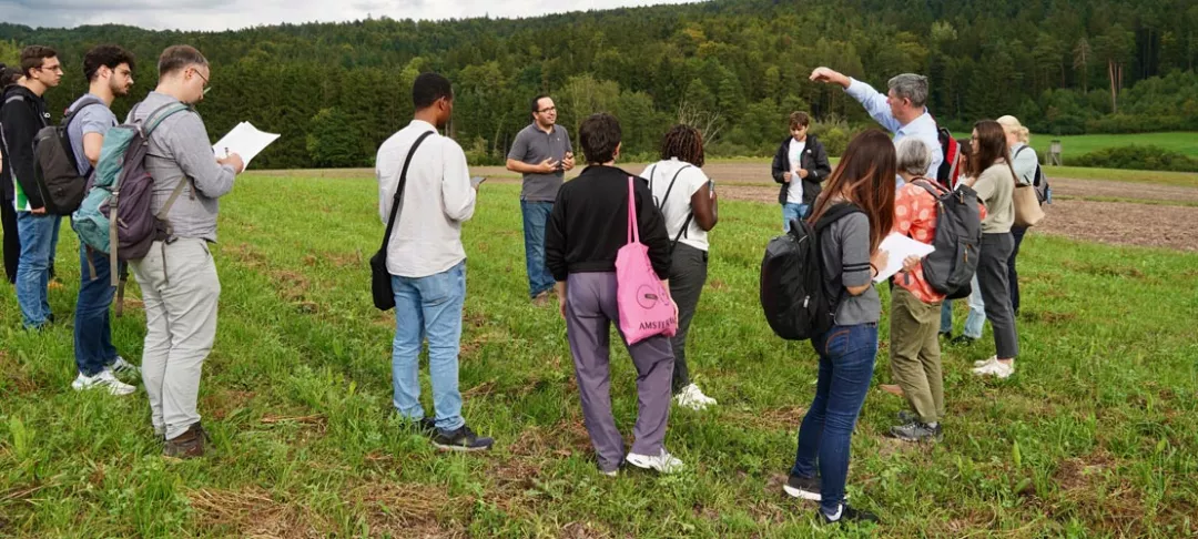 People listen to a person speaking during a field visit, green, rural scenary in background
