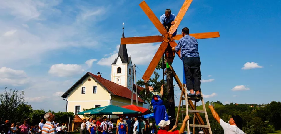 A group of people standing on a ladder setting up a small wooden windmill.