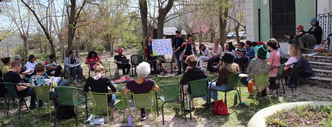 A large group of people sitting in a discussion group outdoors