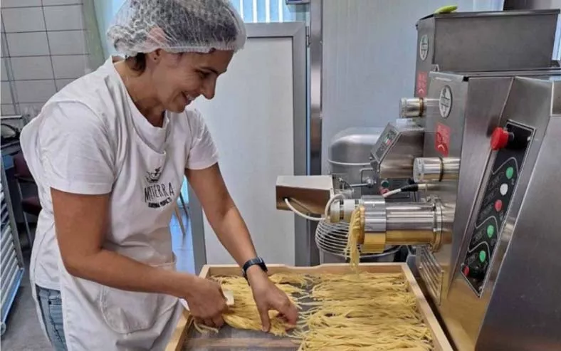 a woman in a white shirt and white apron holding a piece of pasta