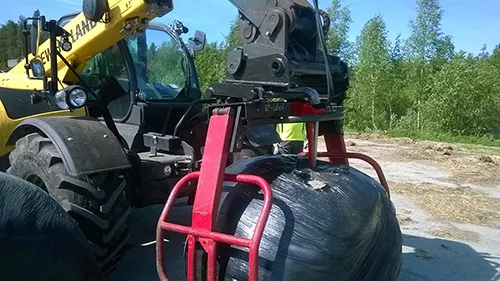 a large black bale in a gripper on the front of a tractor