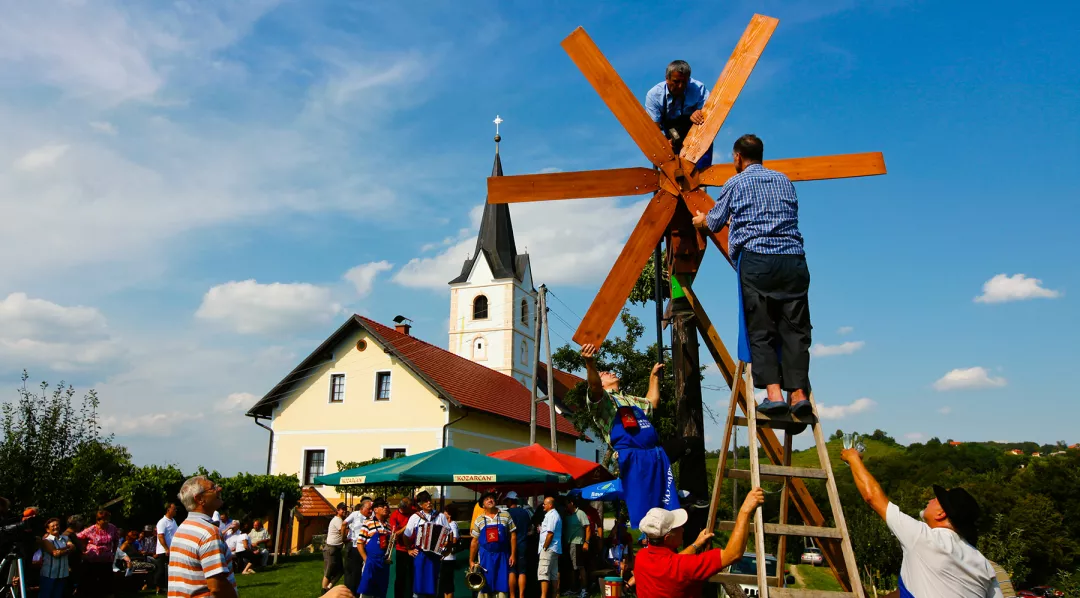 A group of people standing on a ladder setting up a small wooden windmill