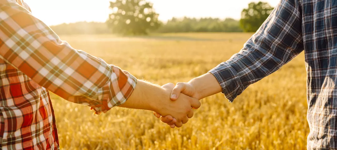 Two farmers in wheat field making agreement with handshake at sunset