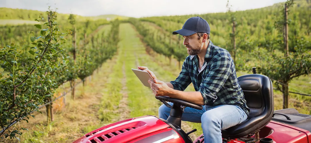 Farmer with tablet sitting on mini tractor