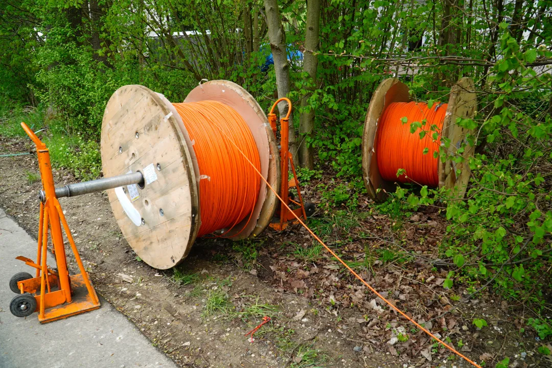 Two large wooden spools of orange cable placed outdoors near a grassy and wooded area
