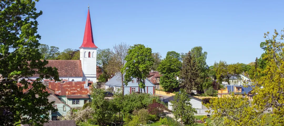 A village with colorful houses, greenery, and a church with a red steeple