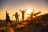 Group of happy friends are standing at mountain top and greeting sunrise or sunset above clouds