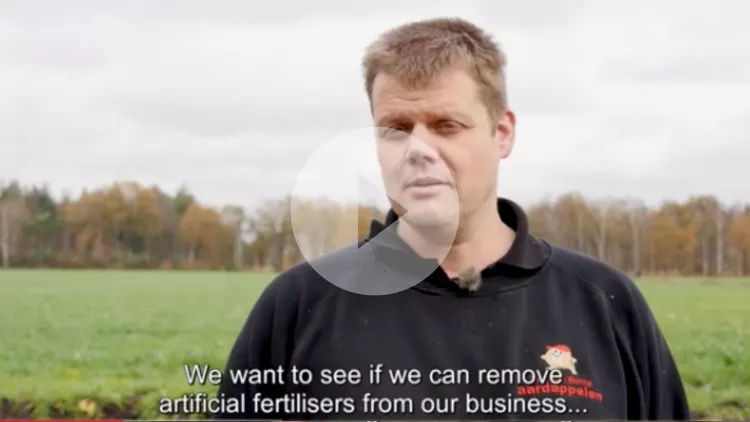 A young, blonde farmer explains his use of fertilisers in front of his field
