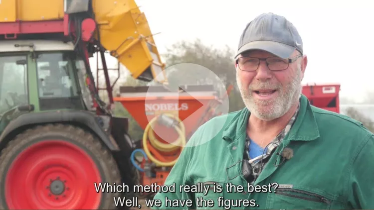 A farmer explains something to the camera in front of his red tractor